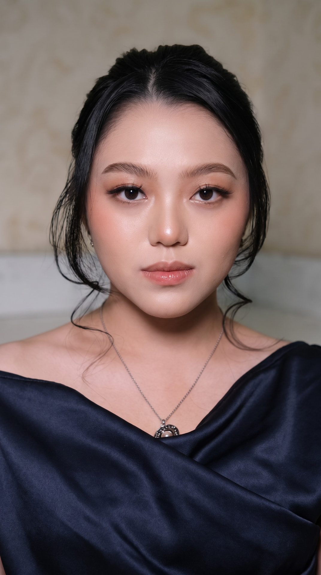Riasan soft glam dengan kulit bercahaya dan sanggul rapi